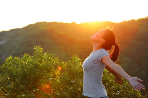 cheering woman open arms at sunrise mountain peak wellness concept-img-blog