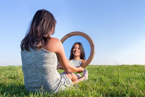 woman sitting on grass looking at her mirror image-img-blog