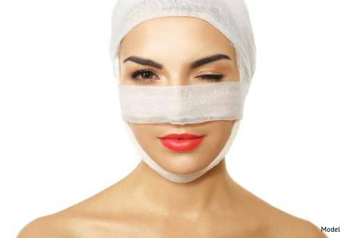 Woman with face wrapped in bandages after plastic surgery.