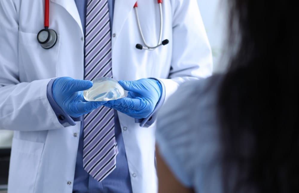 Plastic surgeon holding a breast implant in front of patient.