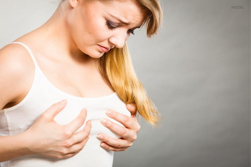 A woman experiencing breast pain as a result of capsular contracture.