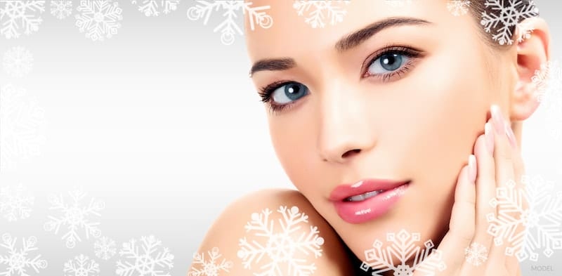 Close up of a young, beautiful woman on a gray background surrounded by snowflakes.