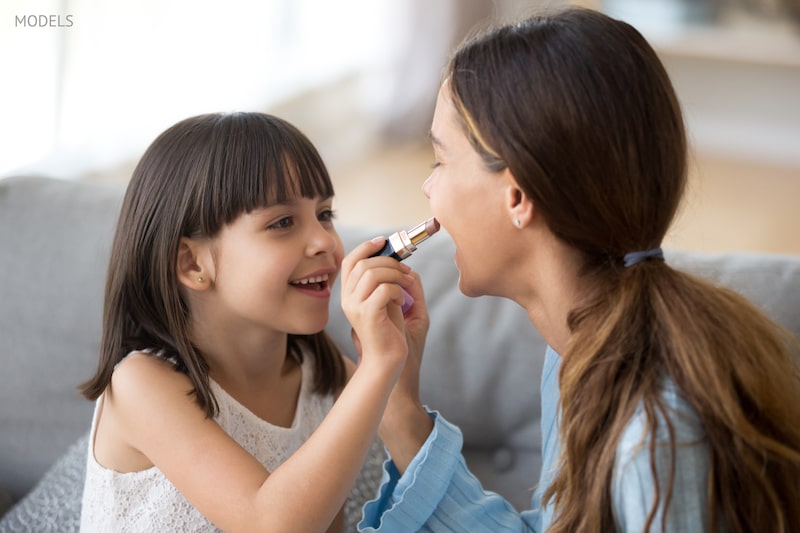 Young daughter putting lipstick on her mother. 
