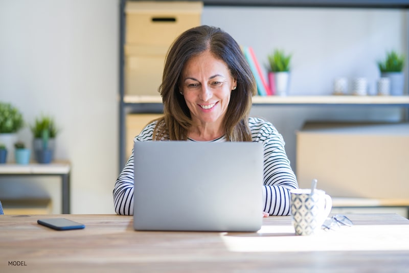 A woman sitting in front of and working on her laptop.