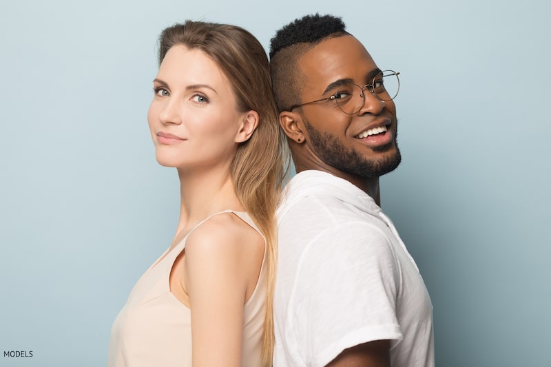White woman and black man standing back-to-back, smiling against a sky blue background.
