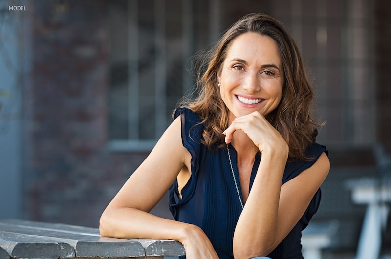 Middle-aged woman sitting at a table, smiling with her hand under her chin.