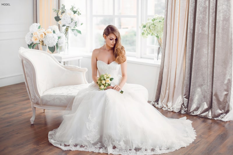 Woman sitting in a wedding dress in front of a window inside