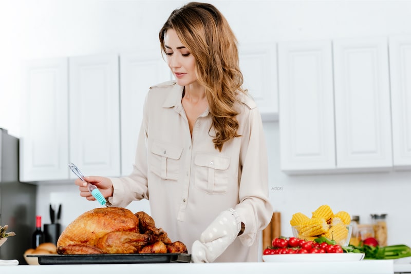 Woman basting a roasted turkey, standing in her kitchen