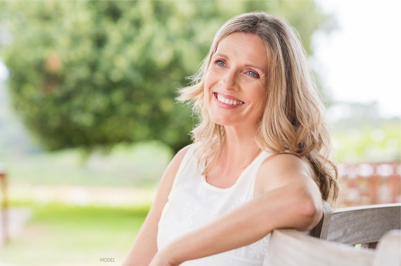 Happy, middle-aged woman sitting on a bench outside.