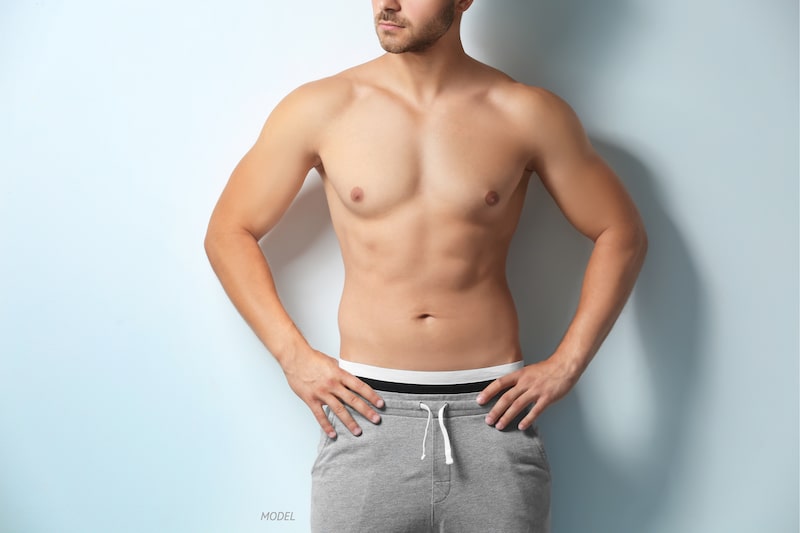 Shirtless man with a toned abdominal contour standing with his arms on his hips.