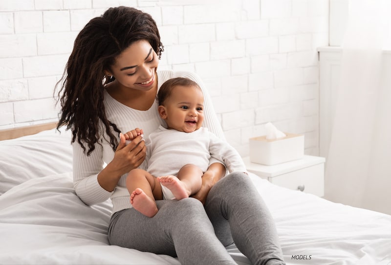 A young mother holding her baby on her lap while sitting on a bed