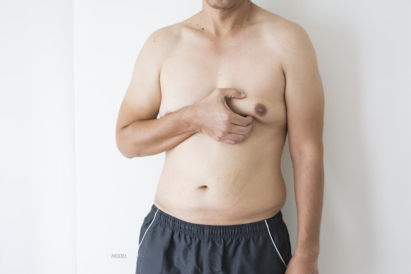 Shirtless male pinching his overly developed breast.