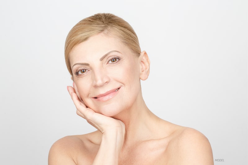 Middle age woman smiling at the camera with her hand on her face