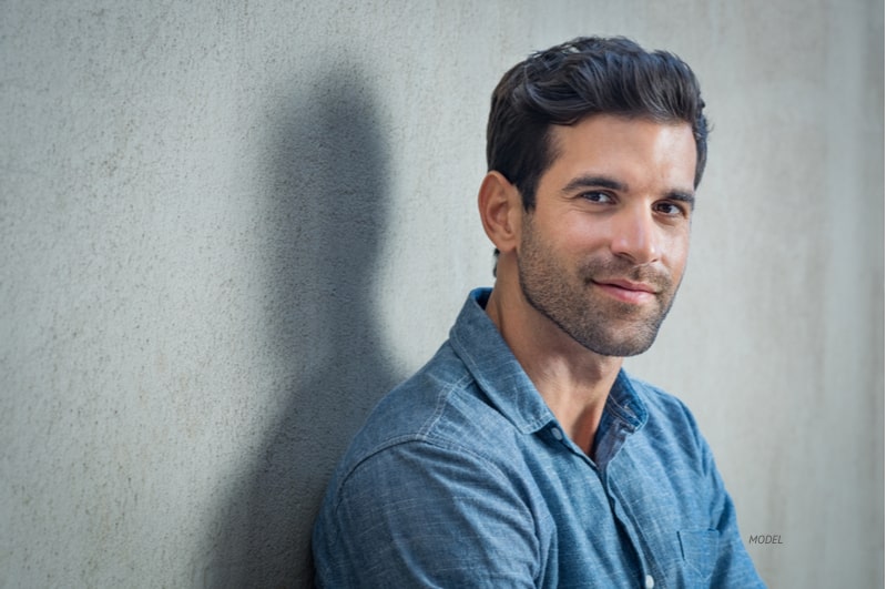 Handsome middle-aged man standing against a wall, looking at the camera.