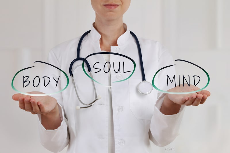 A doctor with hands balancing the words body, mind, and soul.