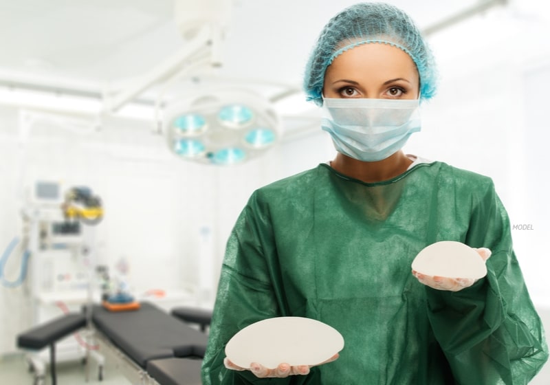  Female surgeon holding large and small breast implants.