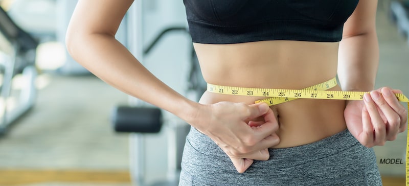 Fit woman measuring her waist.