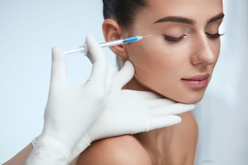 Gloved hands of a skin care professional holding an injectable treatment next to a beautiful woman's face