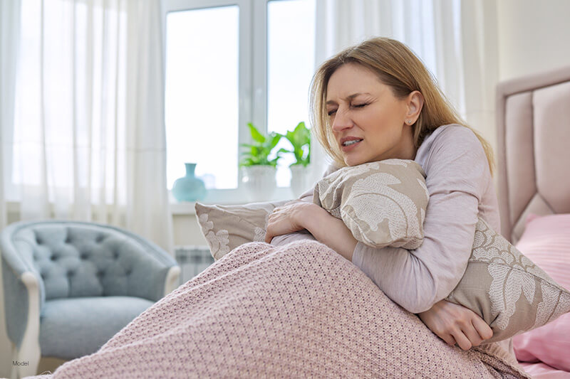 A distressed woman sits in bed holding her pillow.