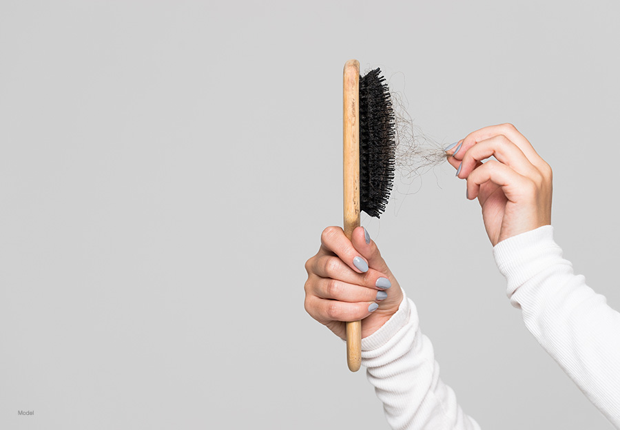 Two arms in white sleeves hold up a brush filled with hair.