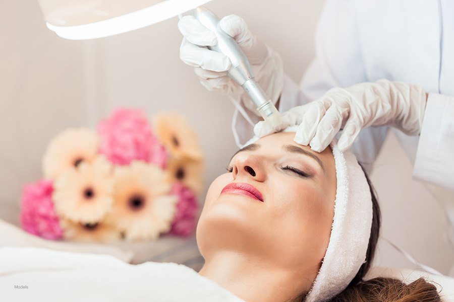 A woman wearing a white terrycloth headband receives a non-surgical facial skin treatment next to pink and off-white flowers.