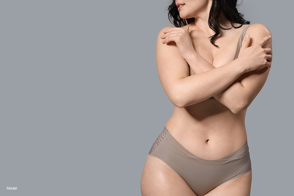 Curvy woman in gray underwear covering her breasts with her arms